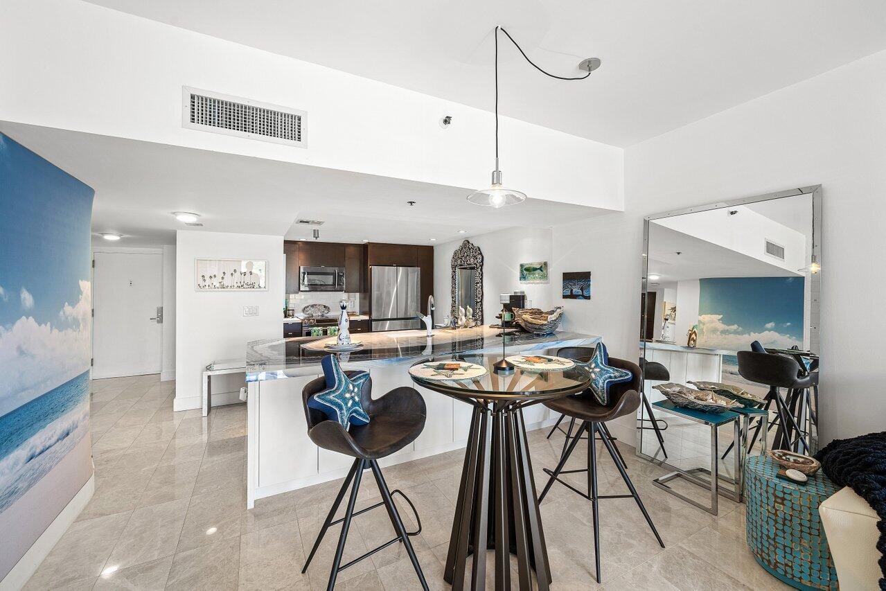 A kitchen with a breakfast bar and a glass-topped dining table sits in an apartment — 901 E Camino Real # 1c, Boca Raton FL 33432, BOCA RATON, FL