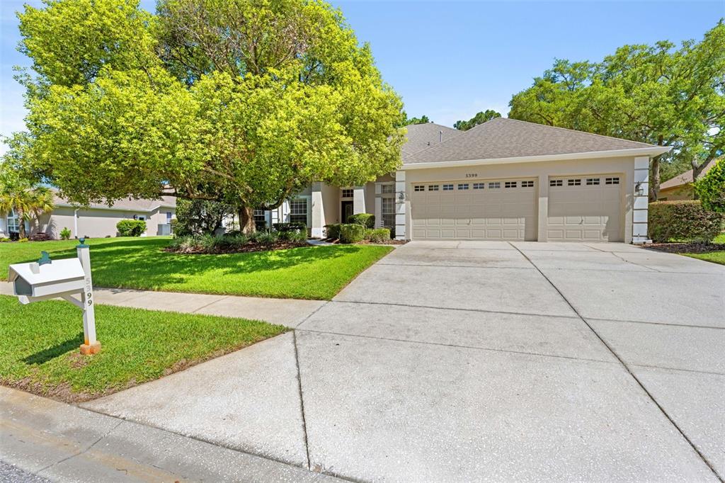 A single-story house with a beige exterior, a three-car garage, and a large front tree — 5399 CHAMPIONSHIP CUP LANE, SPRING HILL, FL