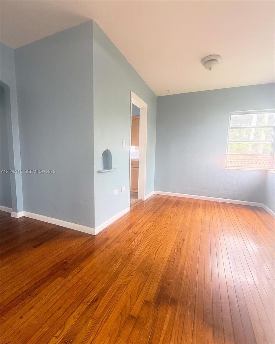 An empty room features light blue walls, hardwood flooring, and a small arched wall niche — 1730 Marseille Dr, Miami Beach FL 33141, MIAMI BEACH, FL