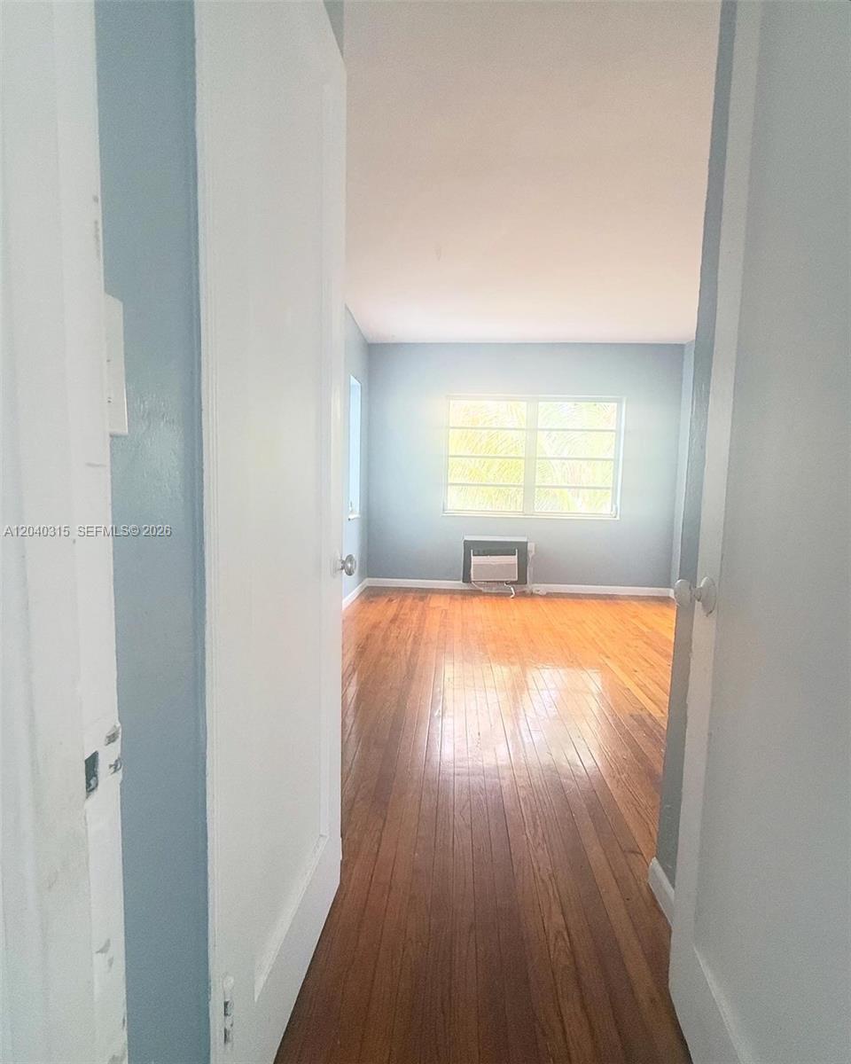 A view through a doorway into a bedroom with hardwood floors and a window unit — 1730 Marseille Dr, Miami Beach FL 33141, MIAMI BEACH, FL