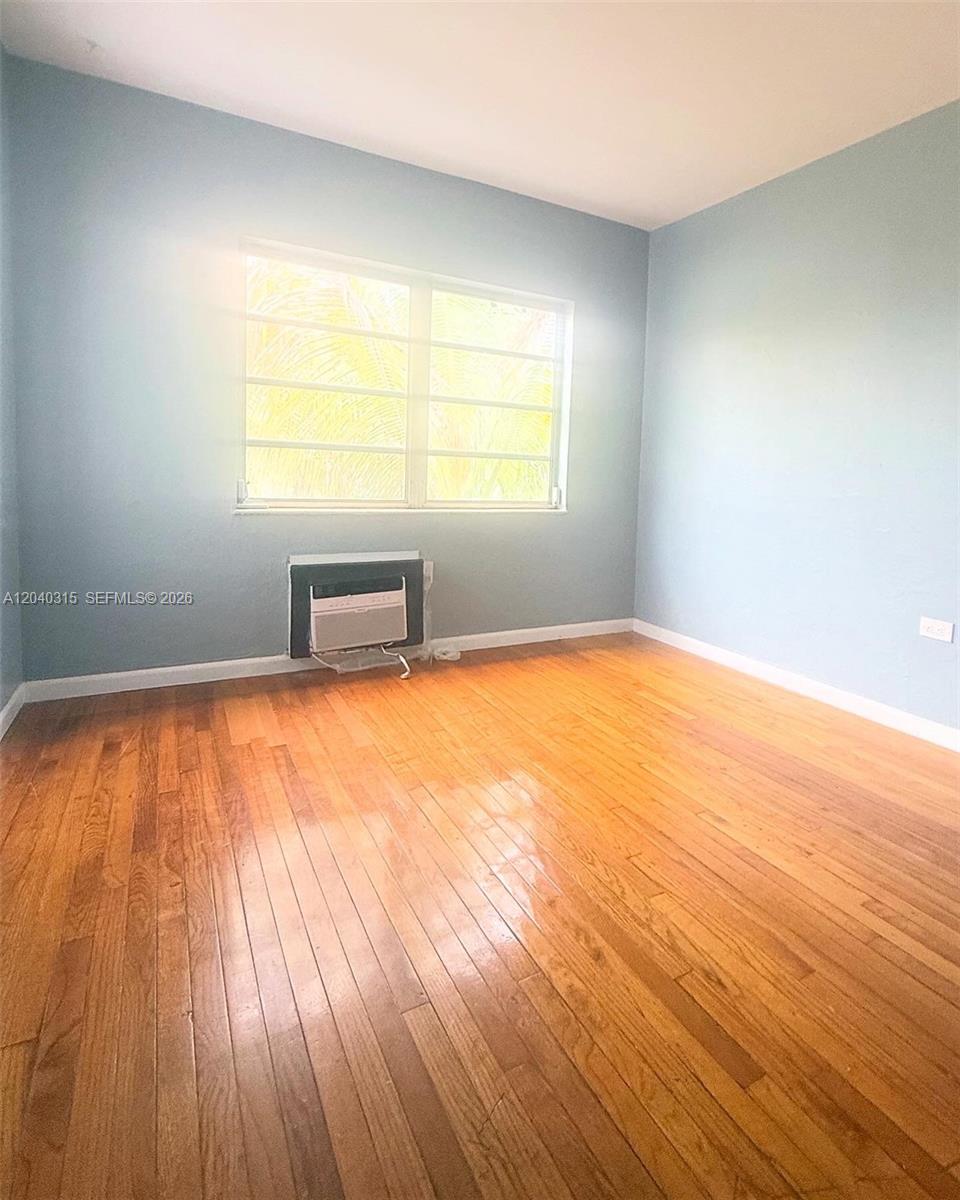 This empty bedroom features light blue walls, hardwood floors, and a window air conditioning unit — 1730 Marseille Dr, Miami Beach FL 33141, MIAMI BEACH, FL