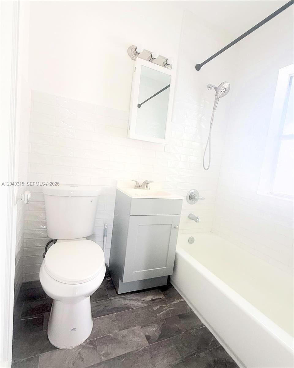 A bathroom features a white toilet, a grey vanity, and a white tiled shower-tub combo — 1730 Marseille Dr, Miami Beach FL 33141, MIAMI BEACH, FL