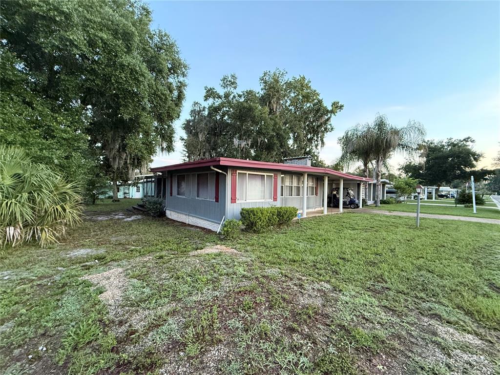 A single-story house with gray siding and a red roof sits on a grassy lot — 103 N TIMBER TRAIL, WILDWOOD, FL