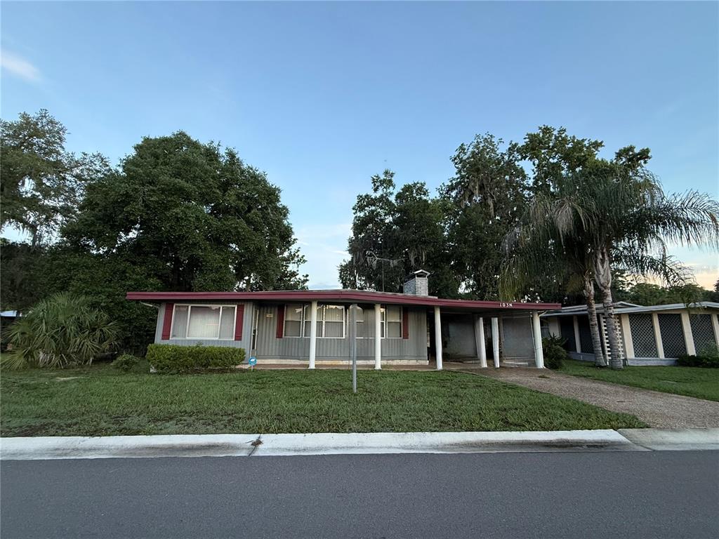 A single-story house with a gray exterior, a covered porch, and a large front lawn — 103 N TIMBER TRAIL, WILDWOOD, FL