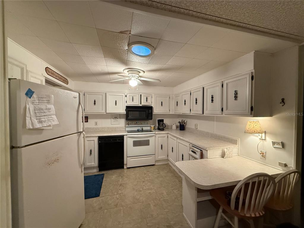 A kitchen features white cabinets, white appliances, a ceiling fan, and a small breakfast bar — 103 N TIMBER TRAIL, WILDWOOD, FL