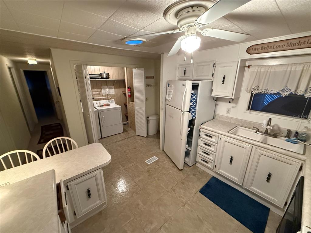 A kitchen with white cabinets, a white refrigerator, and an adjacent laundry closet — 103 N TIMBER TRAIL, WILDWOOD, FL