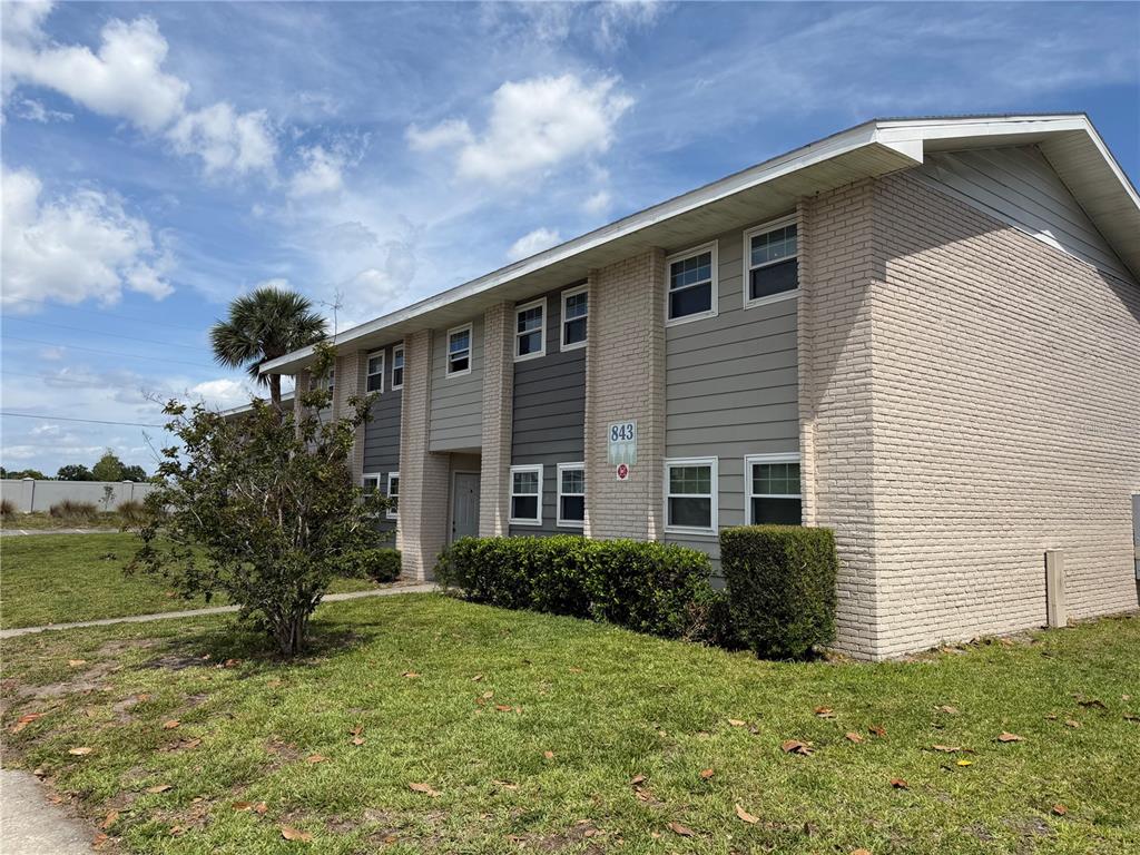 A two-story apartment building features light brick siding, gray accents, and a grassy lawn — 843 SKY LAKE CIRCLE UNIT D, ORLANDO, FL