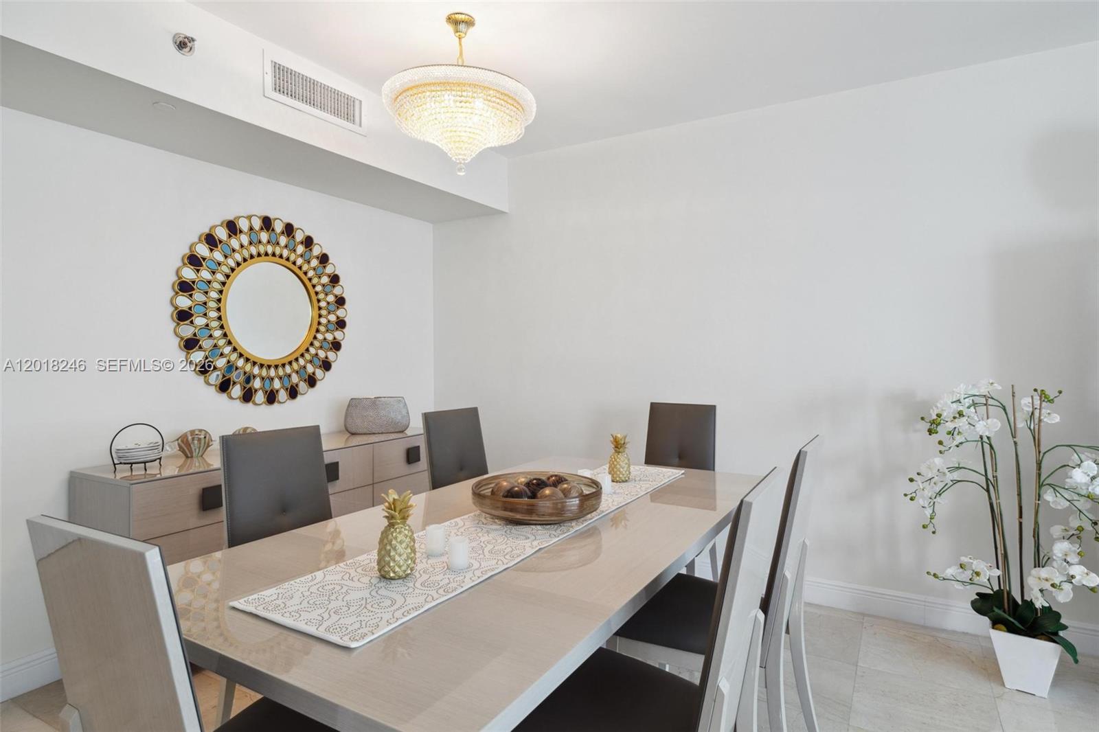 A dining room features a glossy table, gray chairs, a chandelier, and a decorative mirror — 1800 S Ocean Dr # 1005, Hallandale Beach FL 33009, HALLANDALE BEACH, FL