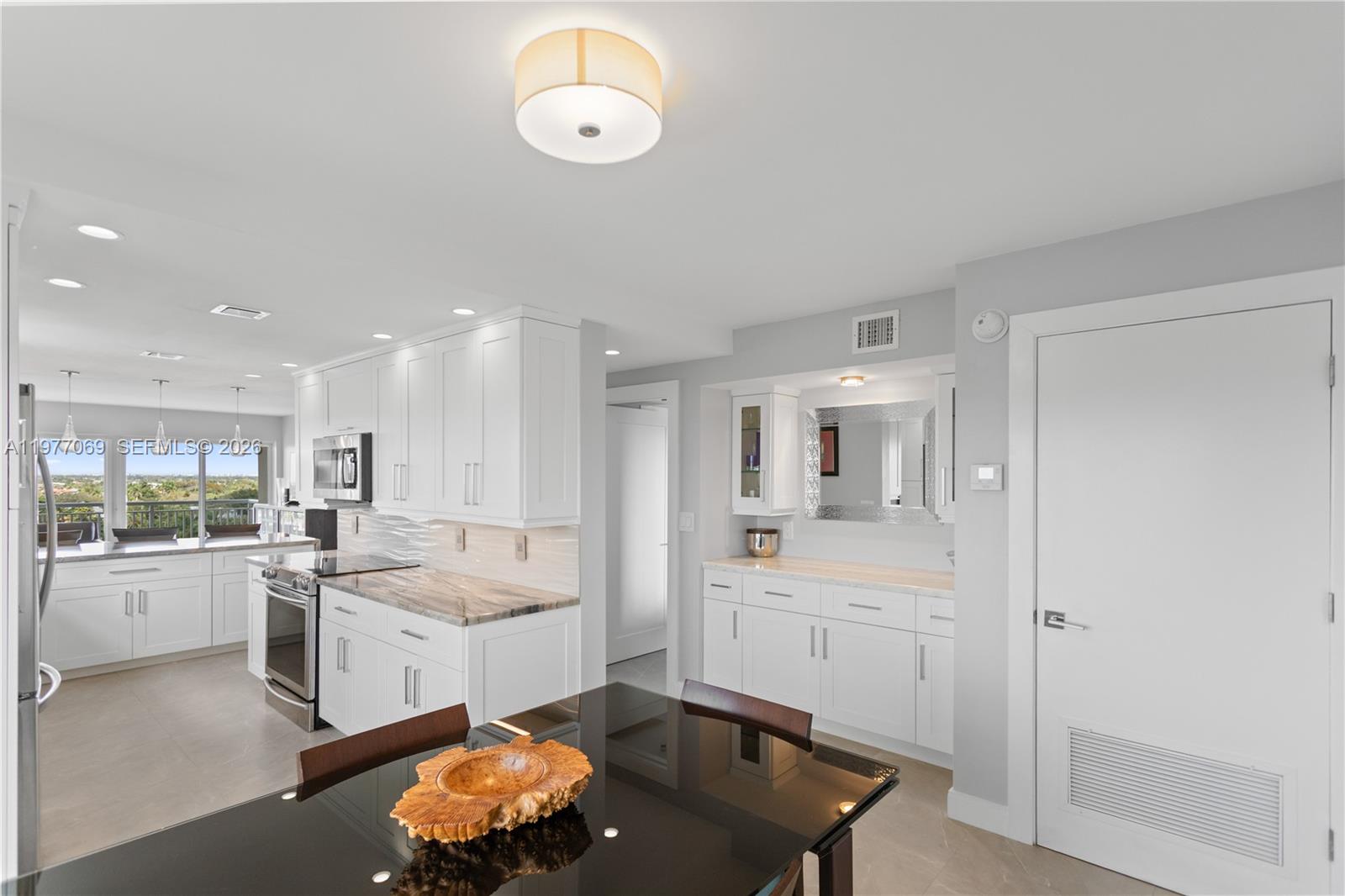 A modern kitchen and dining area feature white cabinets, stone countertops, and a glass table — 2611 N Riverside Dr # 901, Pompano Beach FL 33062, POMPANO BEACH, FL