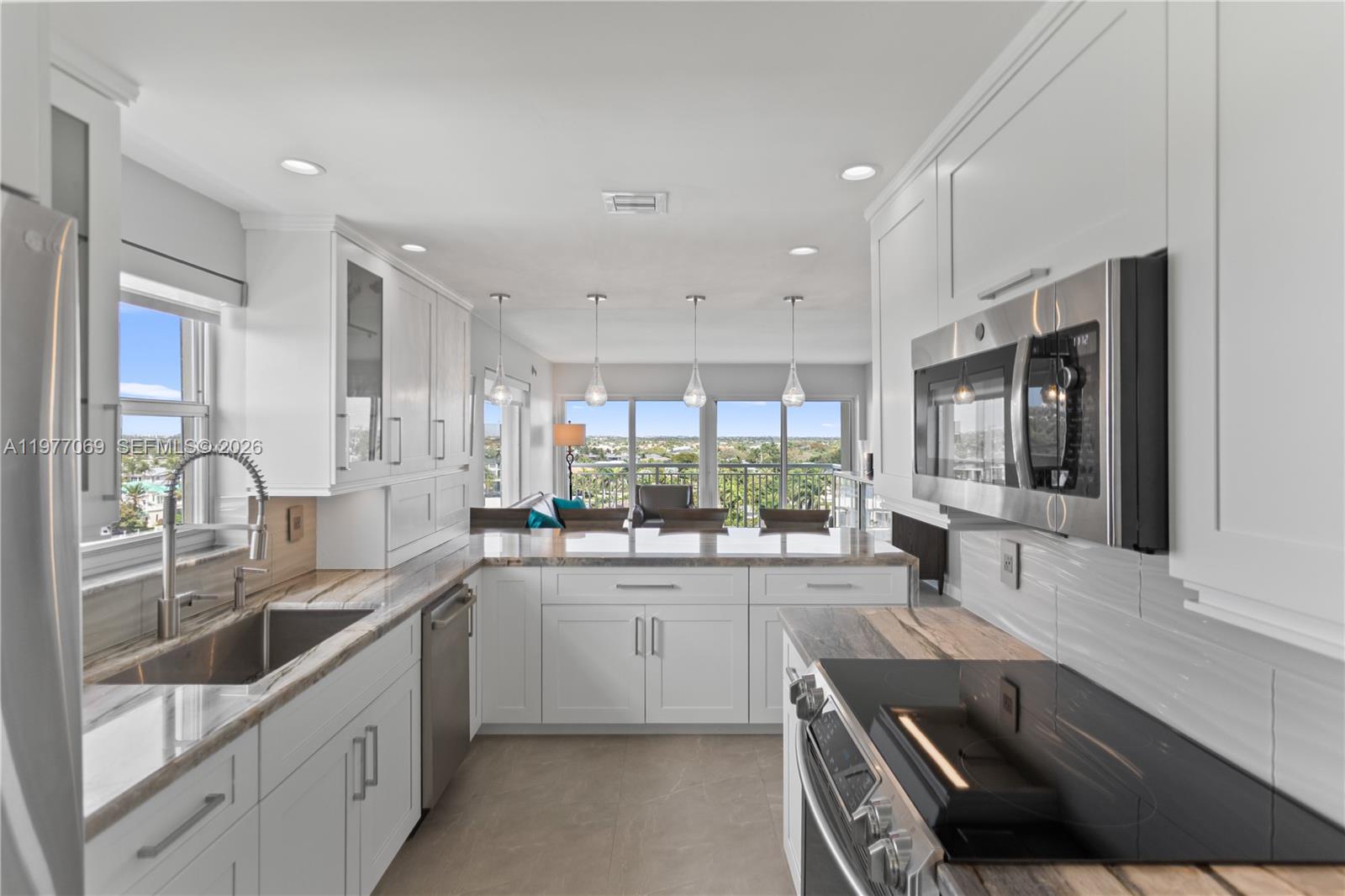A modern kitchen features white cabinets, stone countertops, stainless steel appliances, and a balcony view — 2611 N Riverside Dr # 901, Pompano Beach FL 33062, POMPANO BEACH, FL