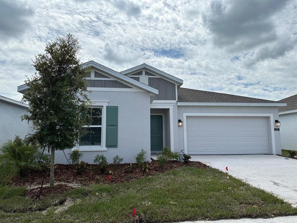 A single-story house with a two-car garage, light gray stucco walls, and green shutters — 652 TROTTERS DRIVE, EAGLE LAKE, FL