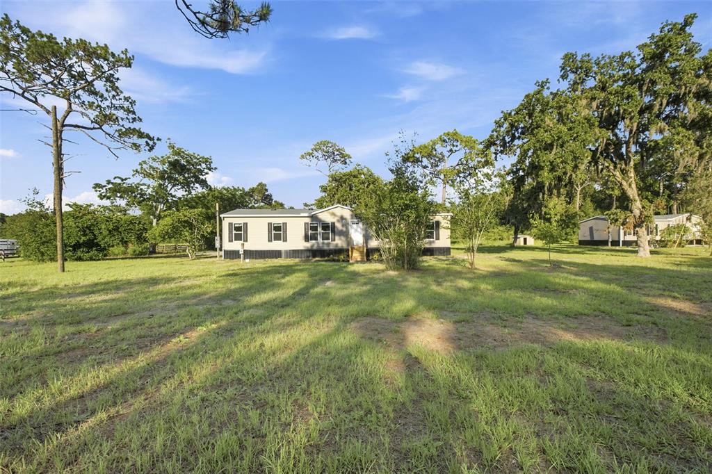 A single-story manufactured home sits on a large, grassy lot with mature trees — 18444 MOORHAVEN DRIVE, SPRING HILL, FL