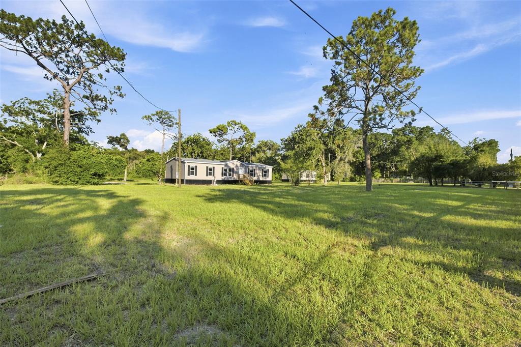 A manufactured home sits on a large, grassy lot surrounded by mature trees — 18444 MOORHAVEN DRIVE, SPRING HILL, FL