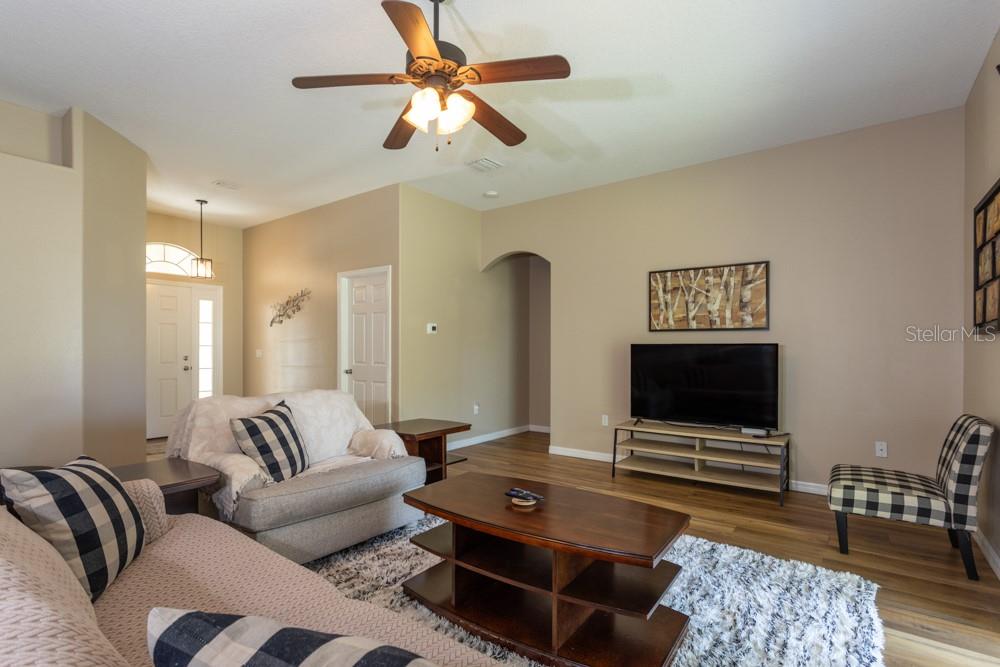 A living room features a ceiling fan, wood-look flooring, a television, and neutral-toned walls — 35 FOXHALL LANE, PALM COAST, FL