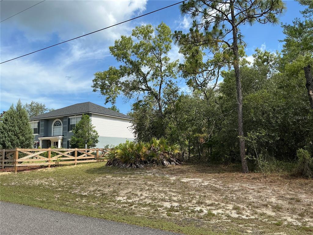 A wooden fence borders a grassy lot next to a two-story house and trees — PERSIMMON AVENUE, WEEKI WACHEE, FL