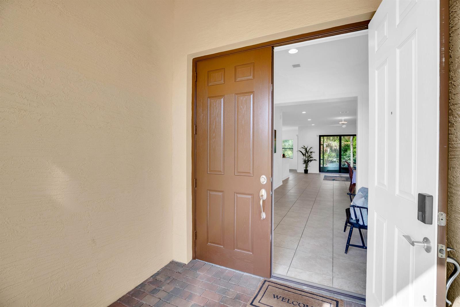 An open brown front door reveals a tiled interior hallway leading to a living area — 5585 40th Avenue, Vero Beach FL 32967, VERO BEACH, FL