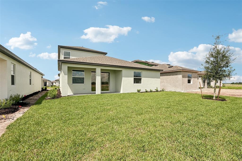 The exterior rear view of a light-colored house features a covered patio and grassy yard — 8712 CANARD COVE, PALMETTO, FL