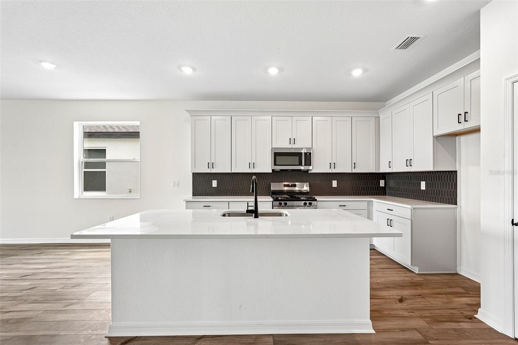 A modern kitchen features white cabinets, a large quartz island, and a dark tiled backsplash — 8712 CANARD COVE, PALMETTO, FL