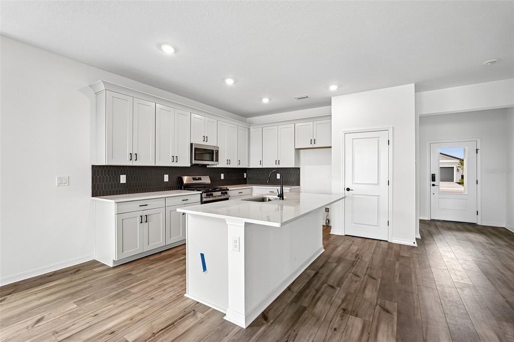A modern kitchen features white cabinets, a central island, dark tile backsplash, and wood flooring — 8712 CANARD COVE, PALMETTO, FL