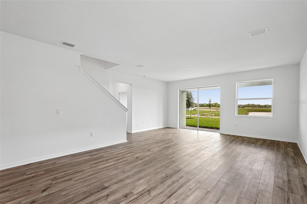 An empty living room with white walls, wood-look flooring, a staircase, and sliding glass doors — 8712 CANARD COVE, PALMETTO, FL