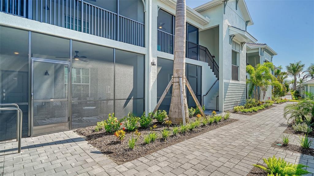A ground-level patio with a screen enclosure sits beside a paved walkway and landscaping — 12550 GALAPAGOS COURT UNIT 106, VENICE, FL