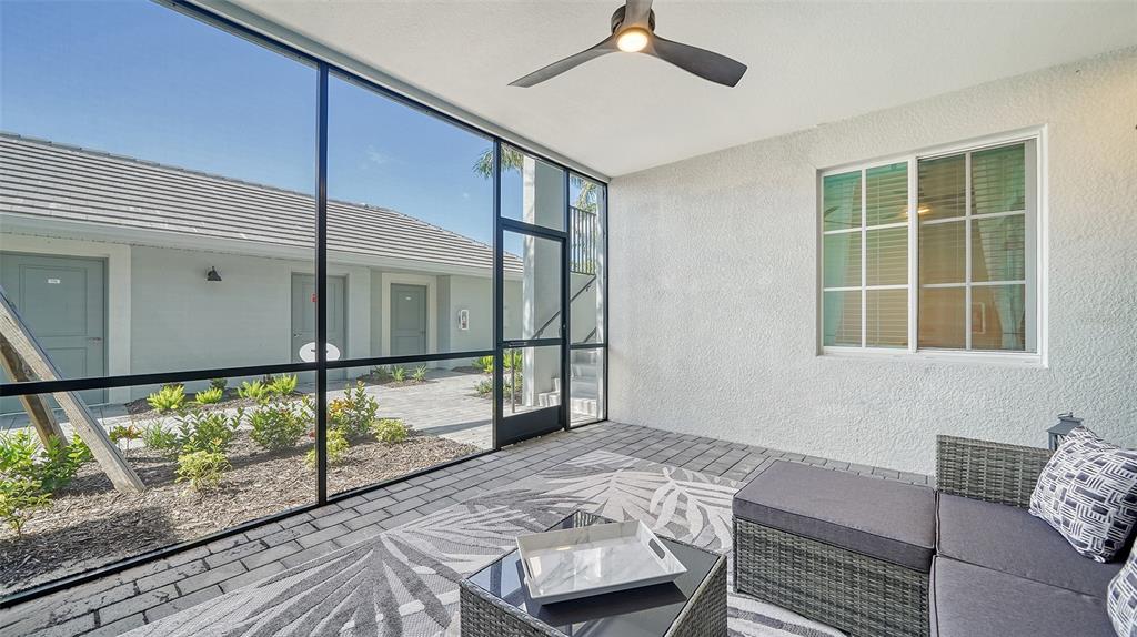 A screened-in patio features a ceiling fan, grey wicker furniture, and a view of buildings — 12550 GALAPAGOS COURT UNIT 106, VENICE, FL