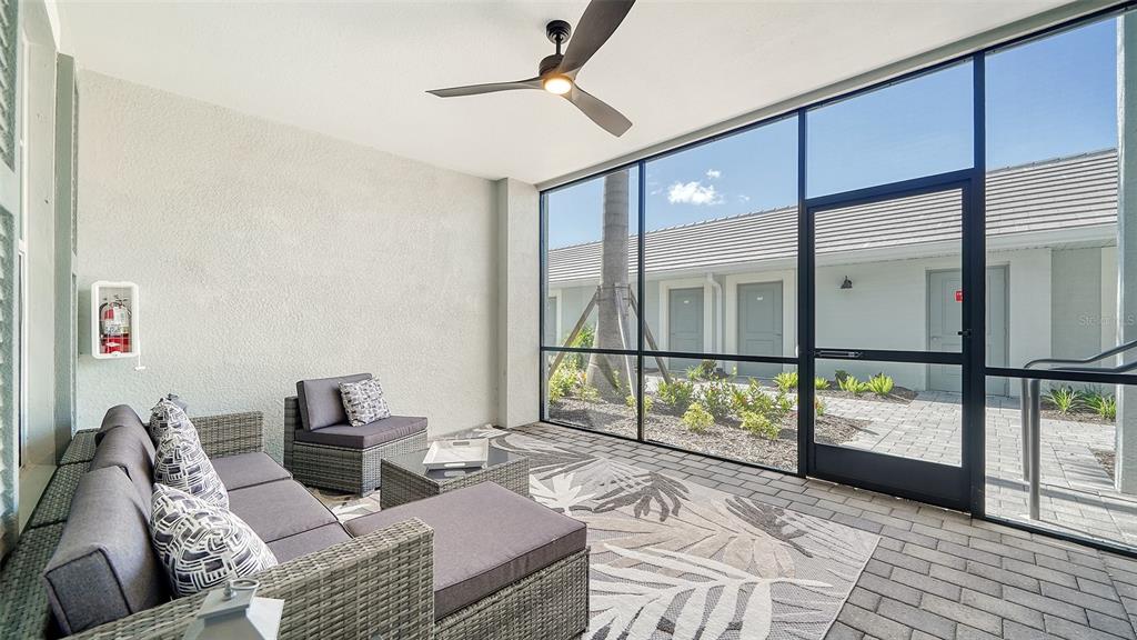 A screened-in patio features gray wicker furniture, a patterned rug, and a ceiling fan — 12550 GALAPAGOS COURT UNIT 106, VENICE, FL