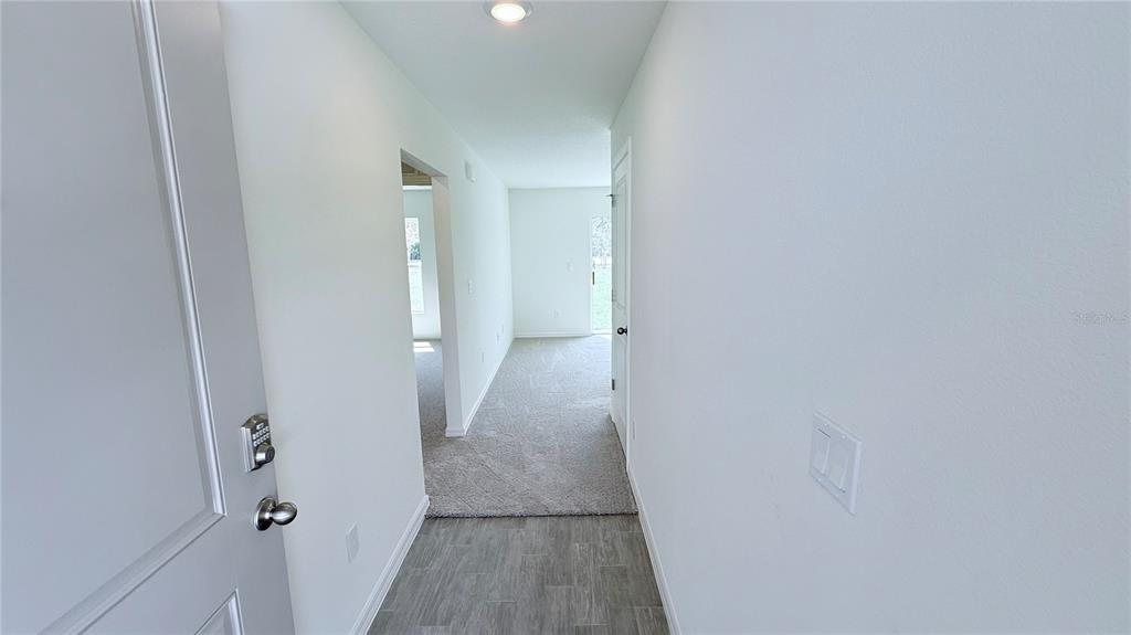 A hallway with gray tile flooring transitions into a carpeted area with white walls — 54 PRINCETON LANE, PALM COAST, FL