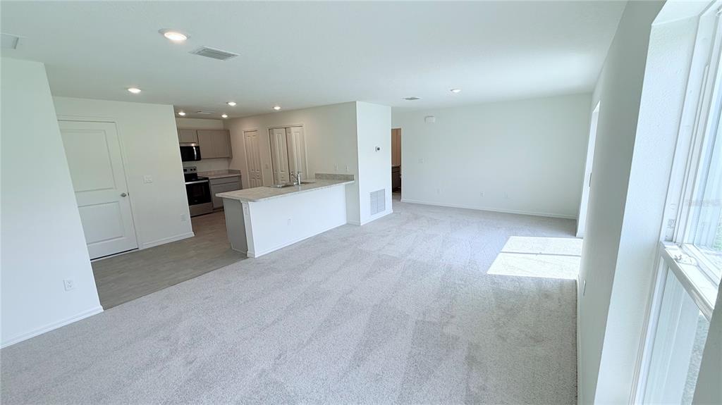 An open-concept living area features gray carpeting, a kitchen with white counters, and recessed lighting — 54 PRINCETON LANE, PALM COAST, FL
