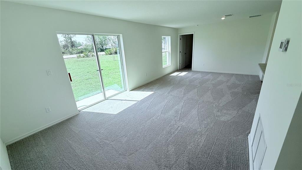 An empty living room features gray wall-to-wall carpeting, white walls, and a sliding glass door — 54 PRINCETON LANE, PALM COAST, FL