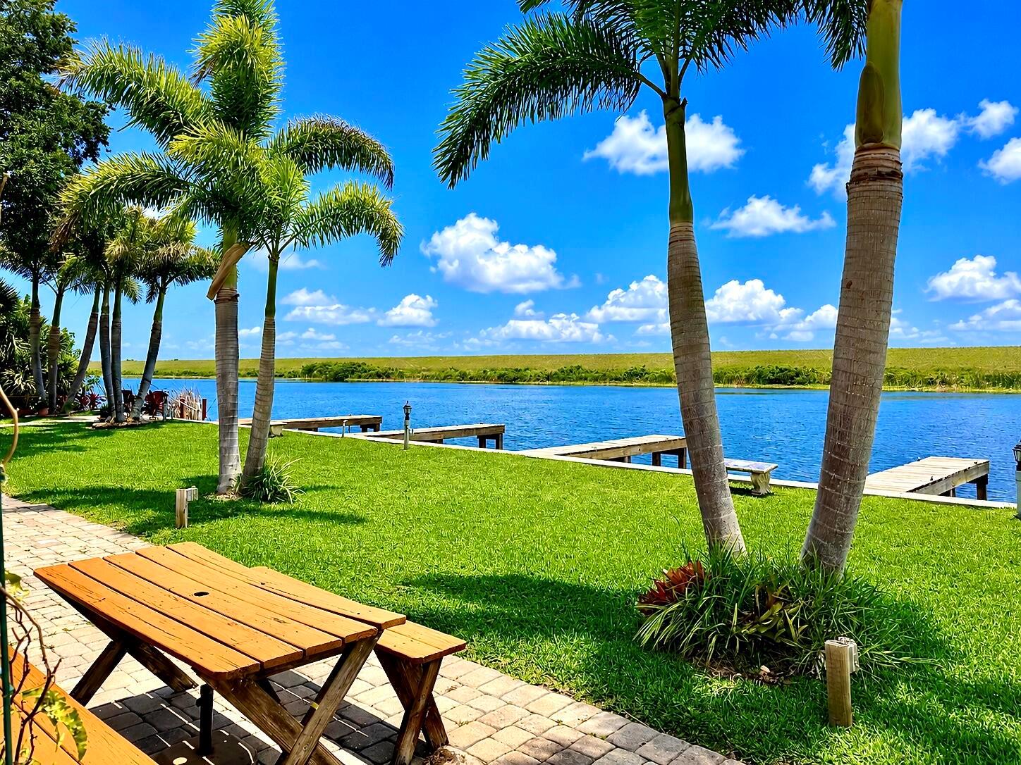 A wooden picnic table sits on a patio overlooking a grassy lawn, docks, and water — 8346 Us-441 # 10, Okeechobee FL 34974, OKEECHOBEE, FL