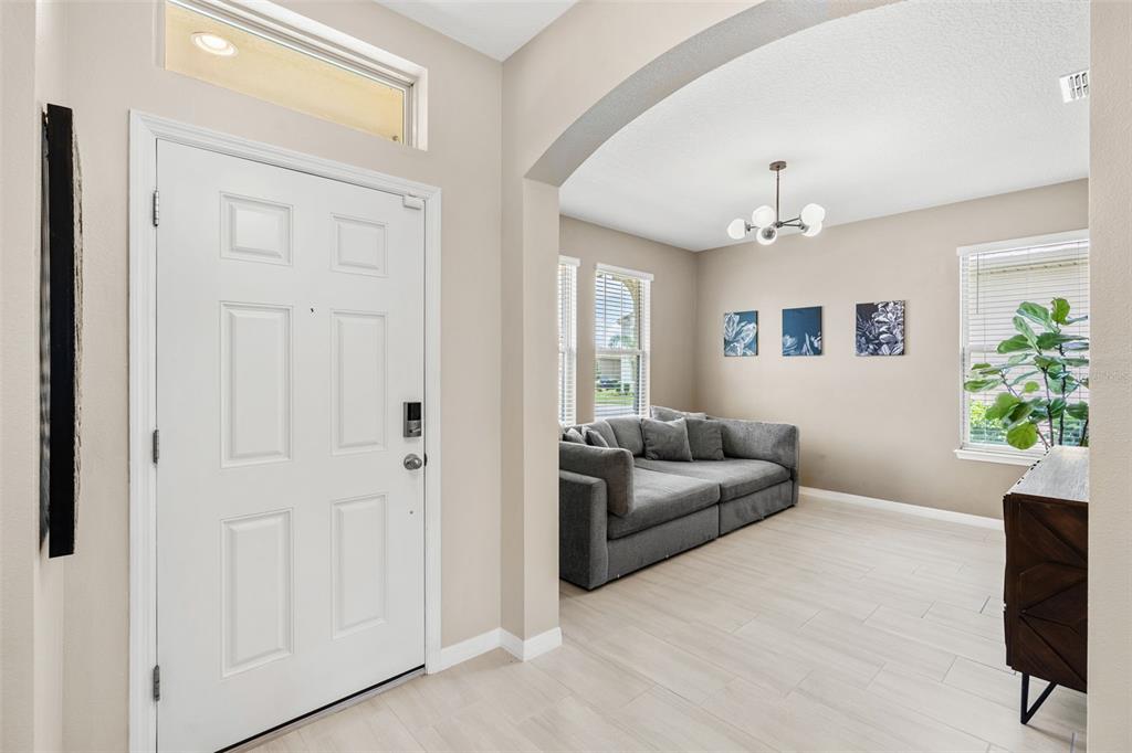 A white front door opens into a living area with light flooring and a gray sofa — 15741 FOUNTAIN SPRINGS ROAD, WINTER GARDEN, FL