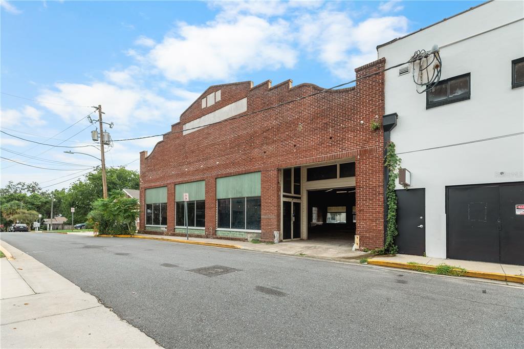 A brick commercial building with large windows and an open garage bay on a street — 113 N 7TH STREET, LEESBURG, FL
