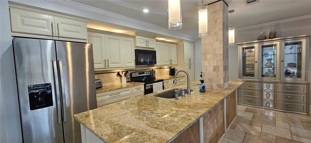 A kitchen features granite countertops, stainless steel appliances, light-colored cabinetry, and a stone-tiled island — 36750 US HIGHWAY 19 N, PALM HARBOR, FL