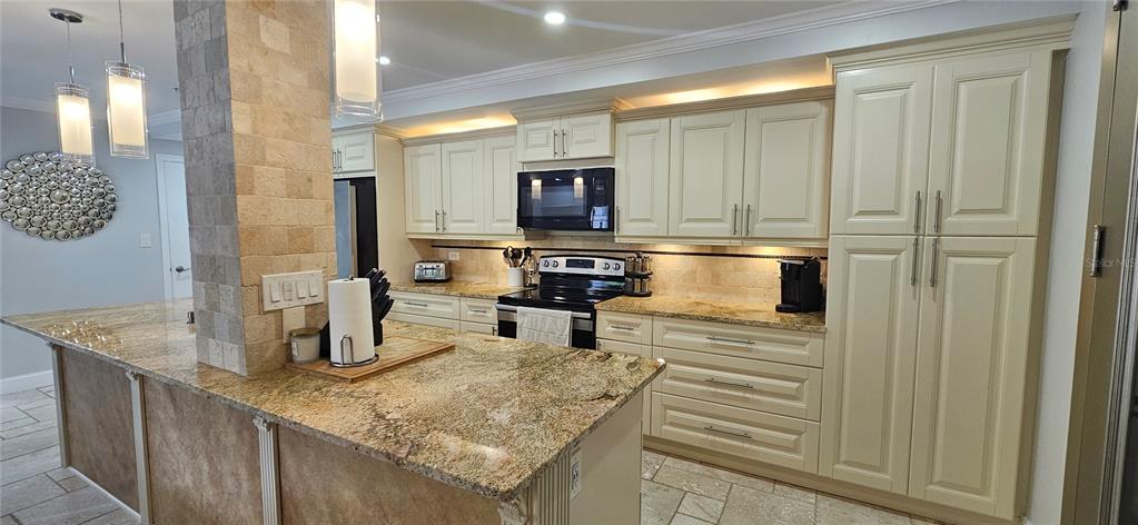 A kitchen features cream-colored cabinets, granite countertops, a stone-tiled pillar, and tile flooring — 36750 US HIGHWAY 19 N, PALM HARBOR, FL