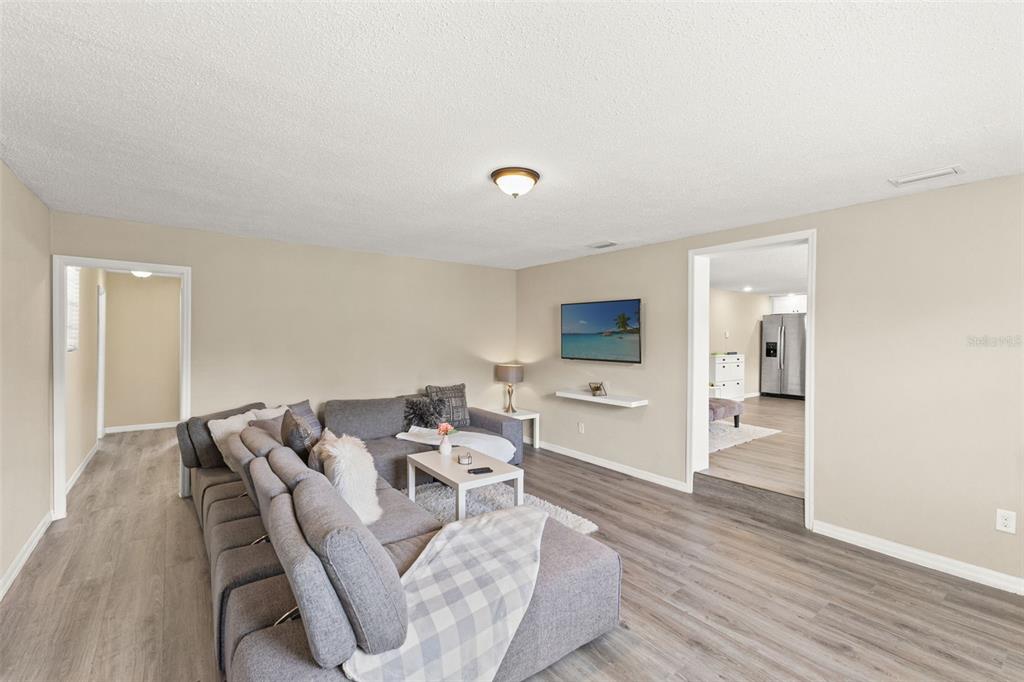 A living room features gray sectional seating, light wood-look flooring, and a wall-mounted television — 7901 N PACKWOOD AVENUE, TAMPA, FL