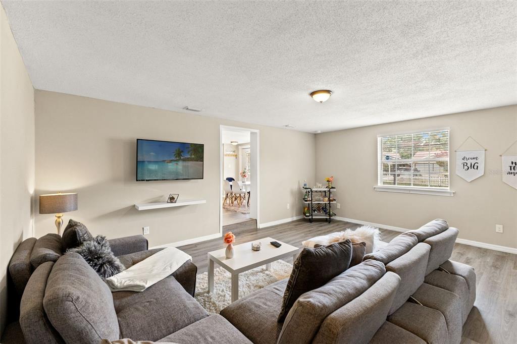 A living room features a grey sectional sofa, a wall-mounted television, and wood-look flooring — 7901 N PACKWOOD AVENUE, TAMPA, FL