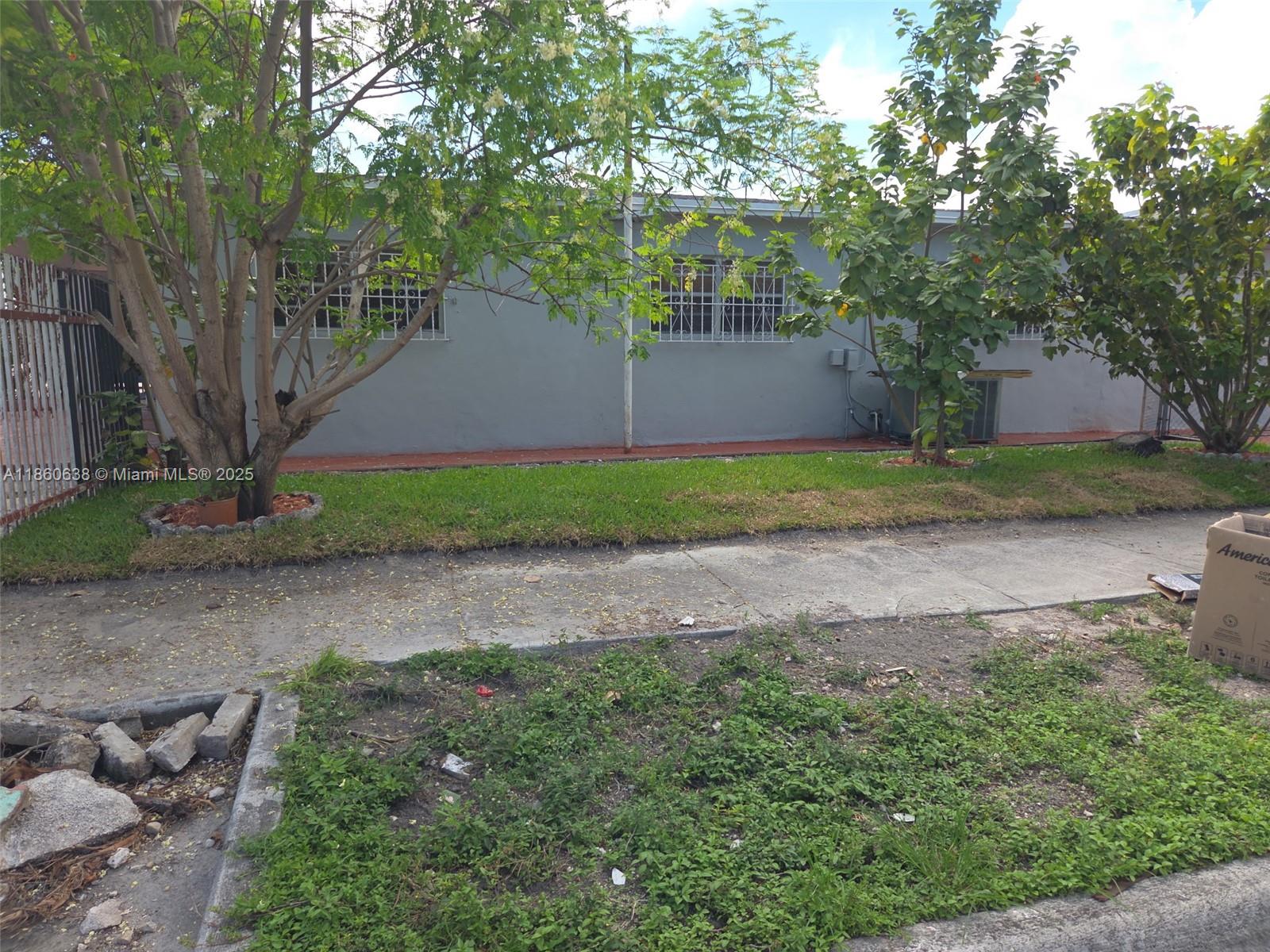 A gray house exterior features a front lawn, sidewalk, and trees under a blue sky — 965 W 23rd St, Hialeah FL 33010, HIALEAH, FL