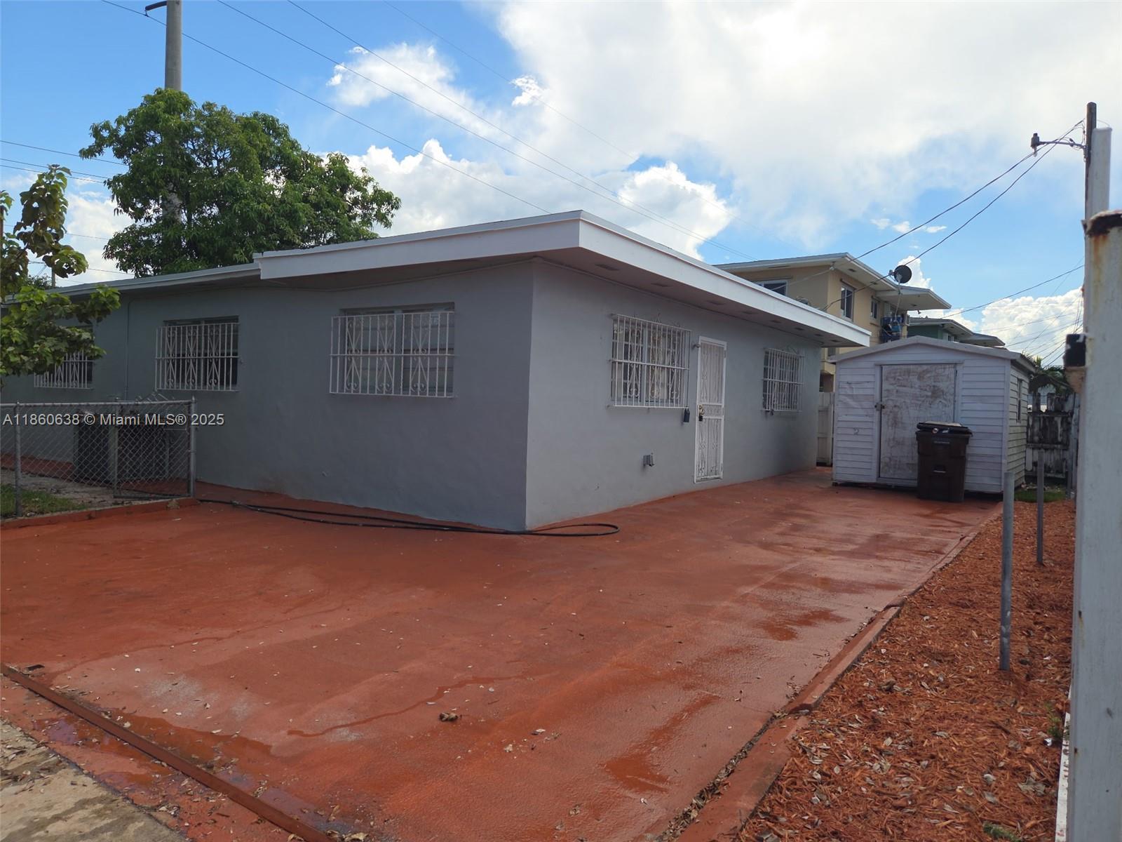 A gray single-story house features a red concrete driveway and a small storage shed — 965 W 23rd St, Hialeah FL 33010, HIALEAH, FL