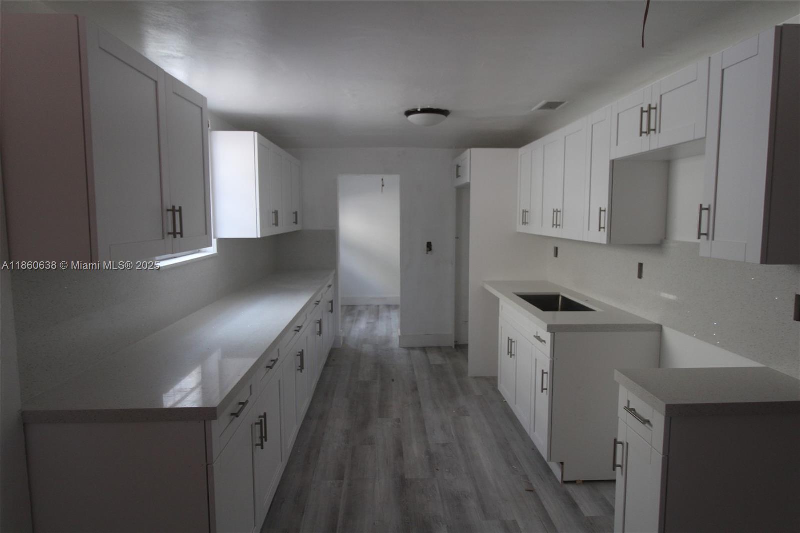 A kitchen features white cabinets, light countertops, and grey wood-look flooring — 965 W 23rd St, Hialeah FL 33010, HIALEAH, FL