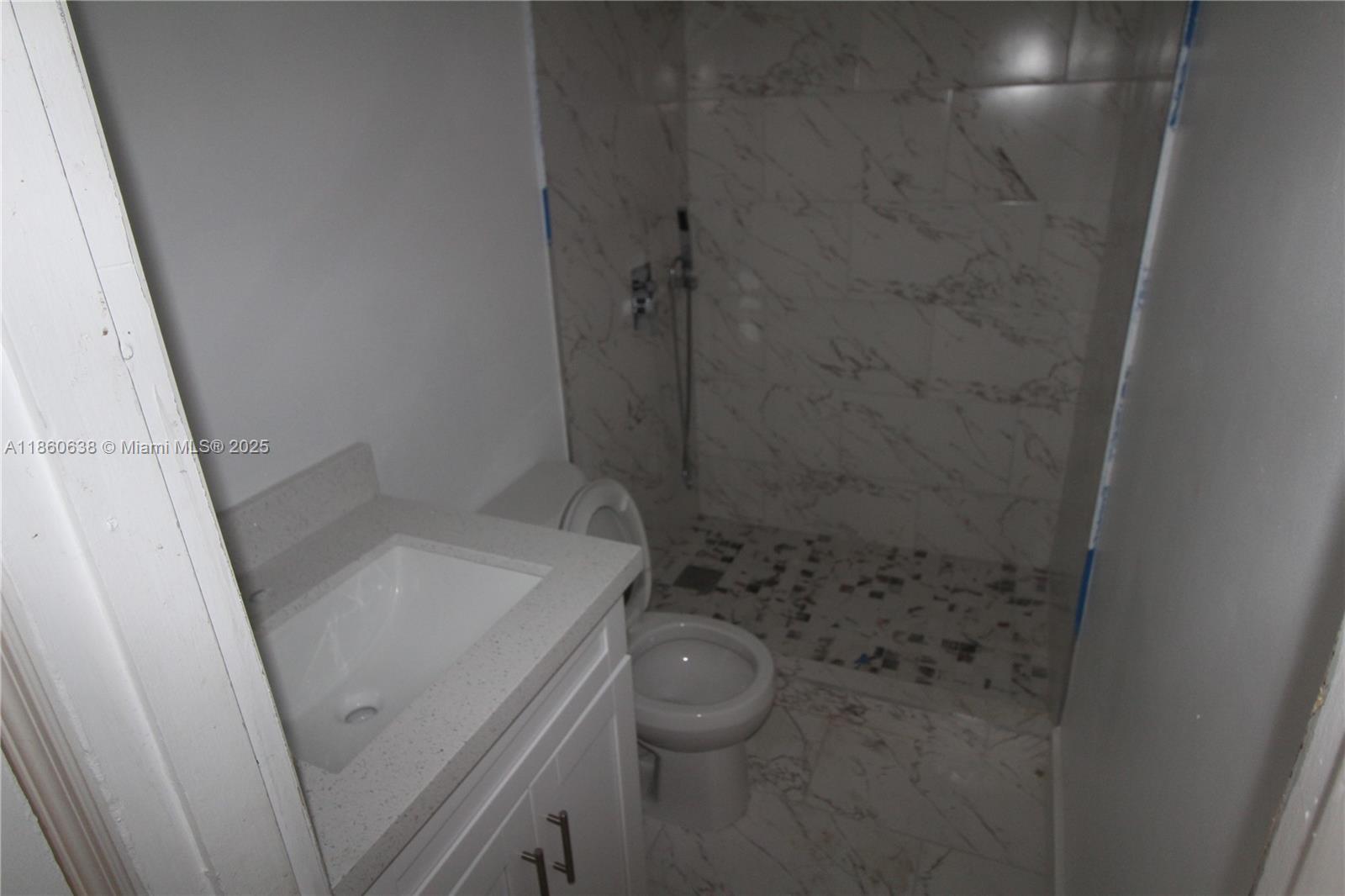 A bathroom features a white vanity, a toilet, and a walk-in shower with marble-style tiles — 965 W 23rd St, Hialeah FL 33010, HIALEAH, FL