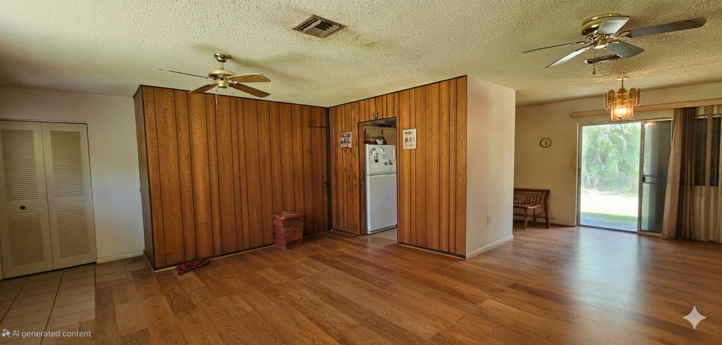 A living room with wood-paneled walls, wood flooring, two ceiling fans, and a sliding glass door — 5675 Sims Road, Delray Beach FL 33484, DELRAY BEACH, FL