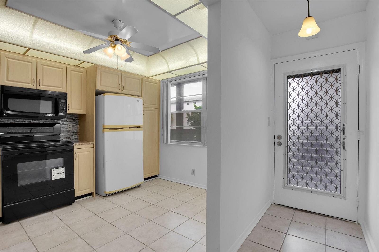 A kitchen with light wood cabinets, black appliances, tile flooring, and an adjacent exterior door — 2006 Granada Drive # N2, Coconut Creek FL 33066, COCONUT CREEK, FL