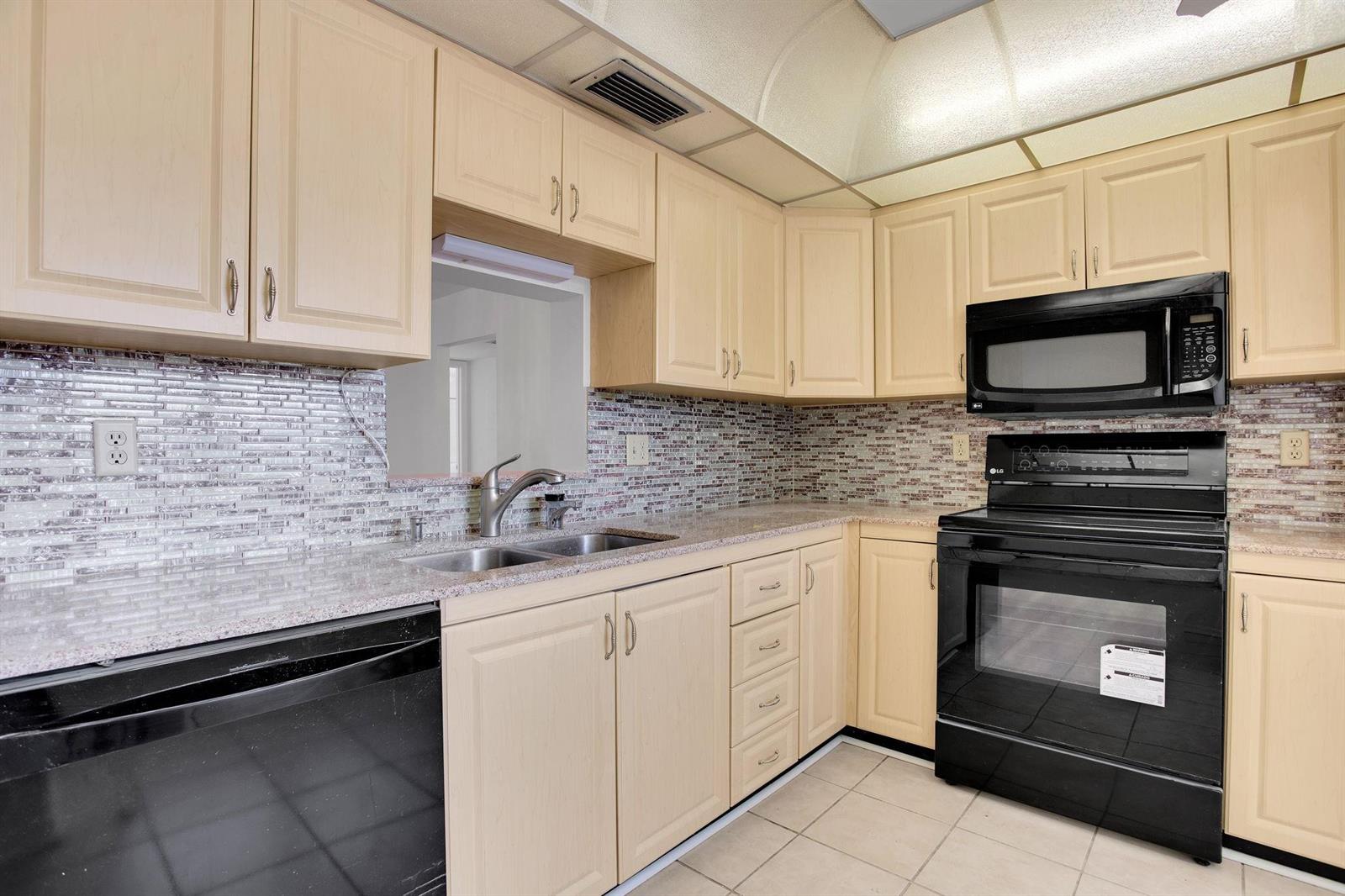 A kitchen with light wood cabinets, black appliances, a tiled backsplash, and granite countertops — 2006 Granada Drive # N2, Coconut Creek FL 33066, COCONUT CREEK, FL