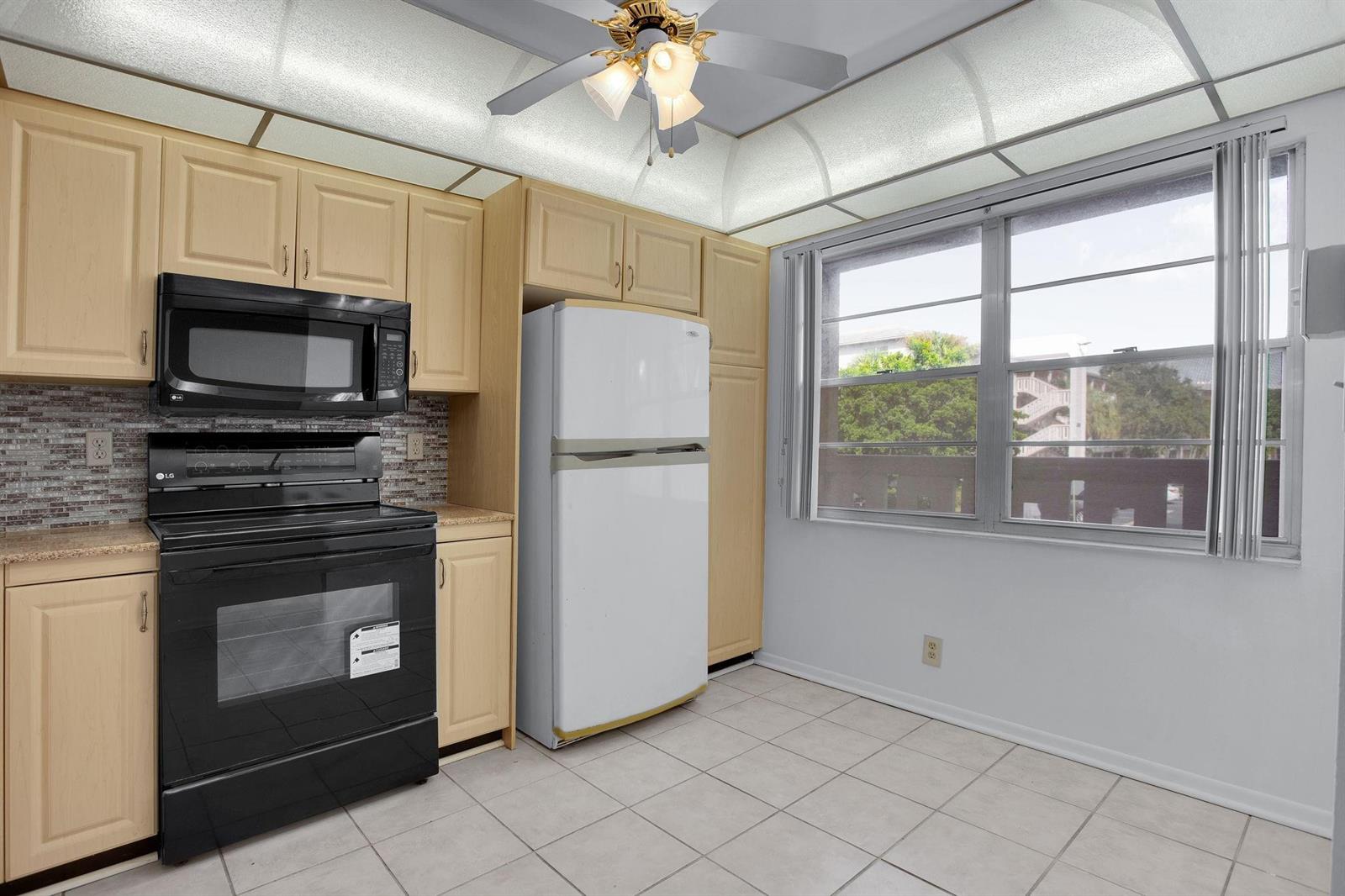 A kitchen with light wood cabinets, black appliances, a white refrigerator, and tiled flooring — 2006 Granada Drive # N2, Coconut Creek FL 33066, COCONUT CREEK, FL