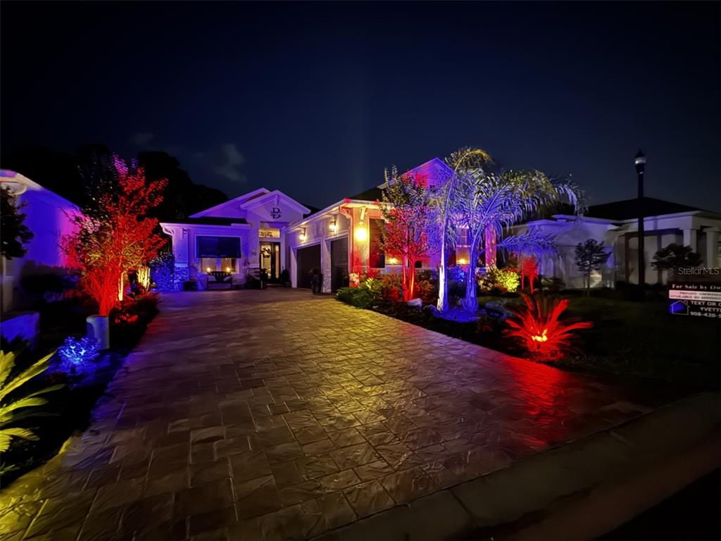 A paved driveway leads to a house illuminated by colorful landscape lighting at night — 20 SPRING STREET, PALM COAST, FL