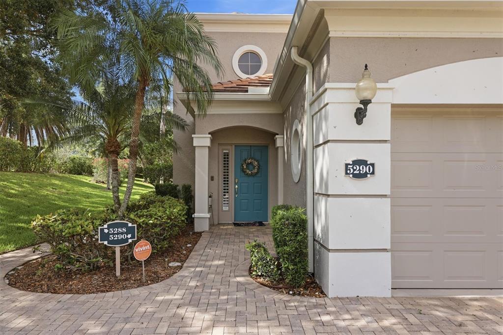 A beige house exterior features a teal front door, a garage, and a paved walkway — 5290 DESCANSO COURT UNIT 201B19, SARASOTA, FL