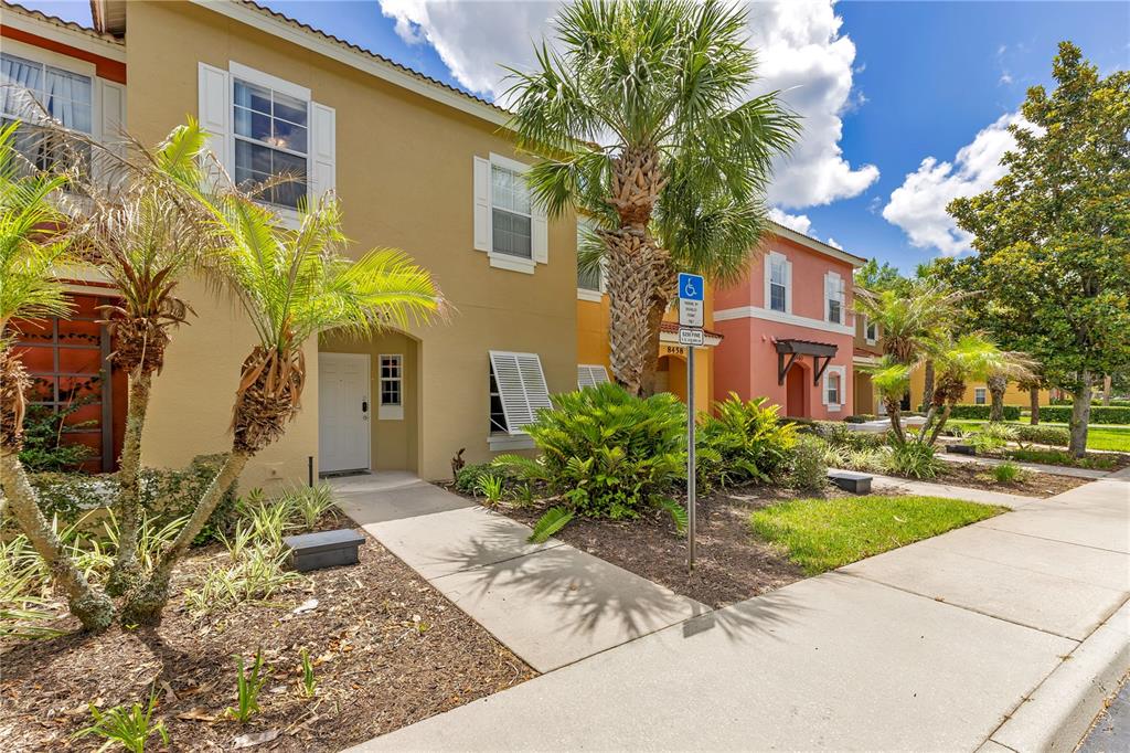 A tan two-story townhouse with a white front door and a palm tree in front — 8456 CRYSTAL COVE LOOP, KISSIMMEE, FL