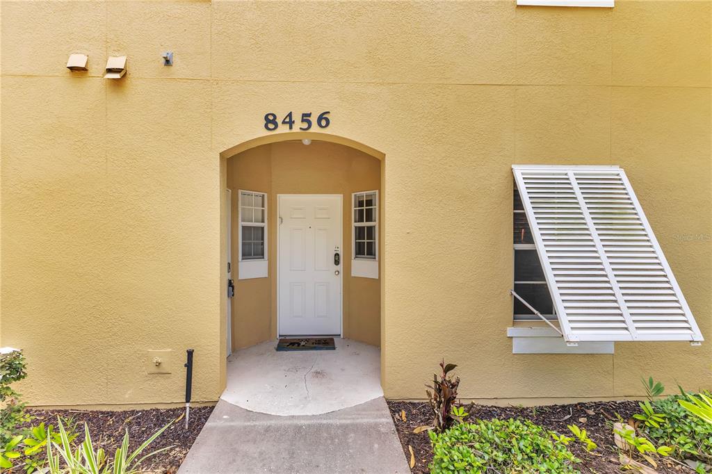 The exterior of a yellow stucco building features a recessed entryway with a white door — 8456 CRYSTAL COVE LOOP, KISSIMMEE, FL