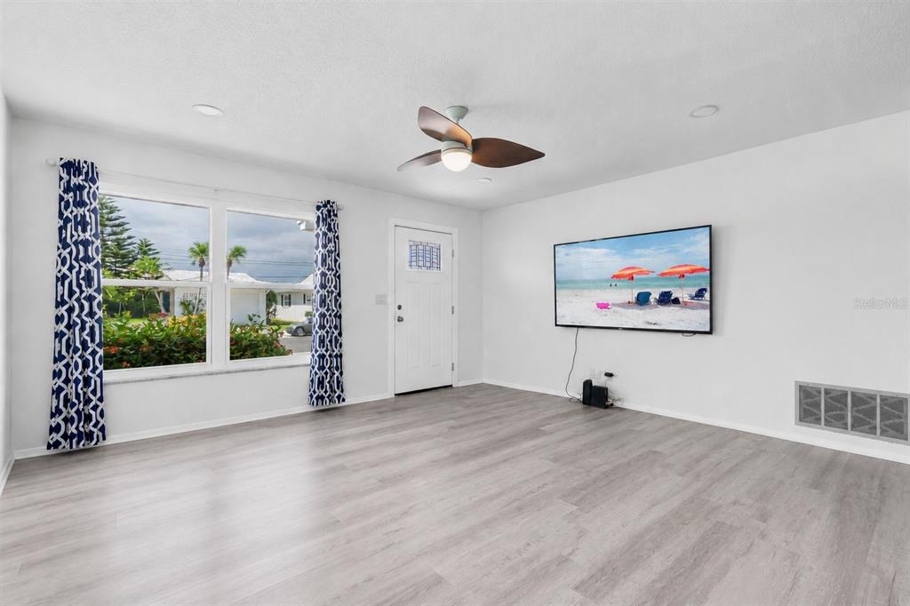 A living room features light wood-look flooring, a ceiling fan, and a wall-mounted television — 3715 98TH AVENUE N UNIT 3, PINELLAS PARK, FL